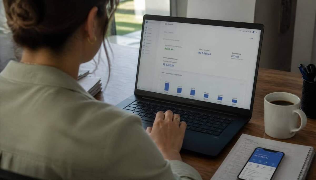 Analista de RH em escritório usando notebook aberto no painel do FGTS Digital, com café e caderno de anotações sobre a mesa em luz natural