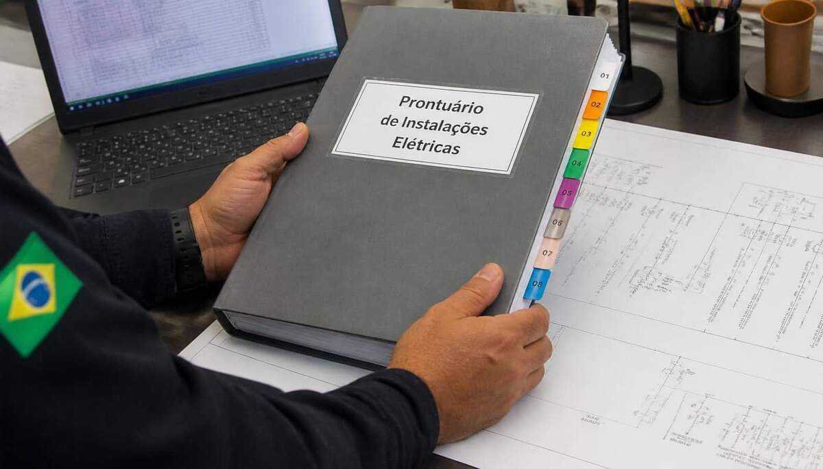 Engenheiro de segurança segurando prontuário de instalações elétricas organizado com divisórias e diagrama unifilar sobre a mesa
