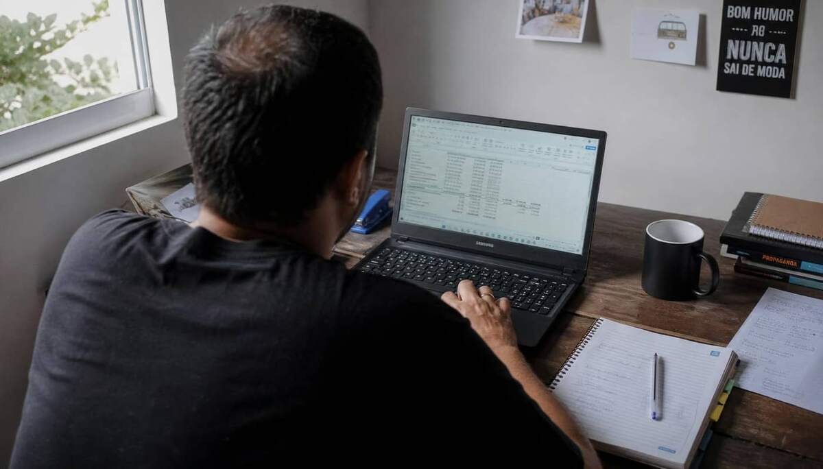 Sócio administrador em home office revisando planilha de cálculo do pró-labore no notebook, com caderno de anotações e café sobre a mesa